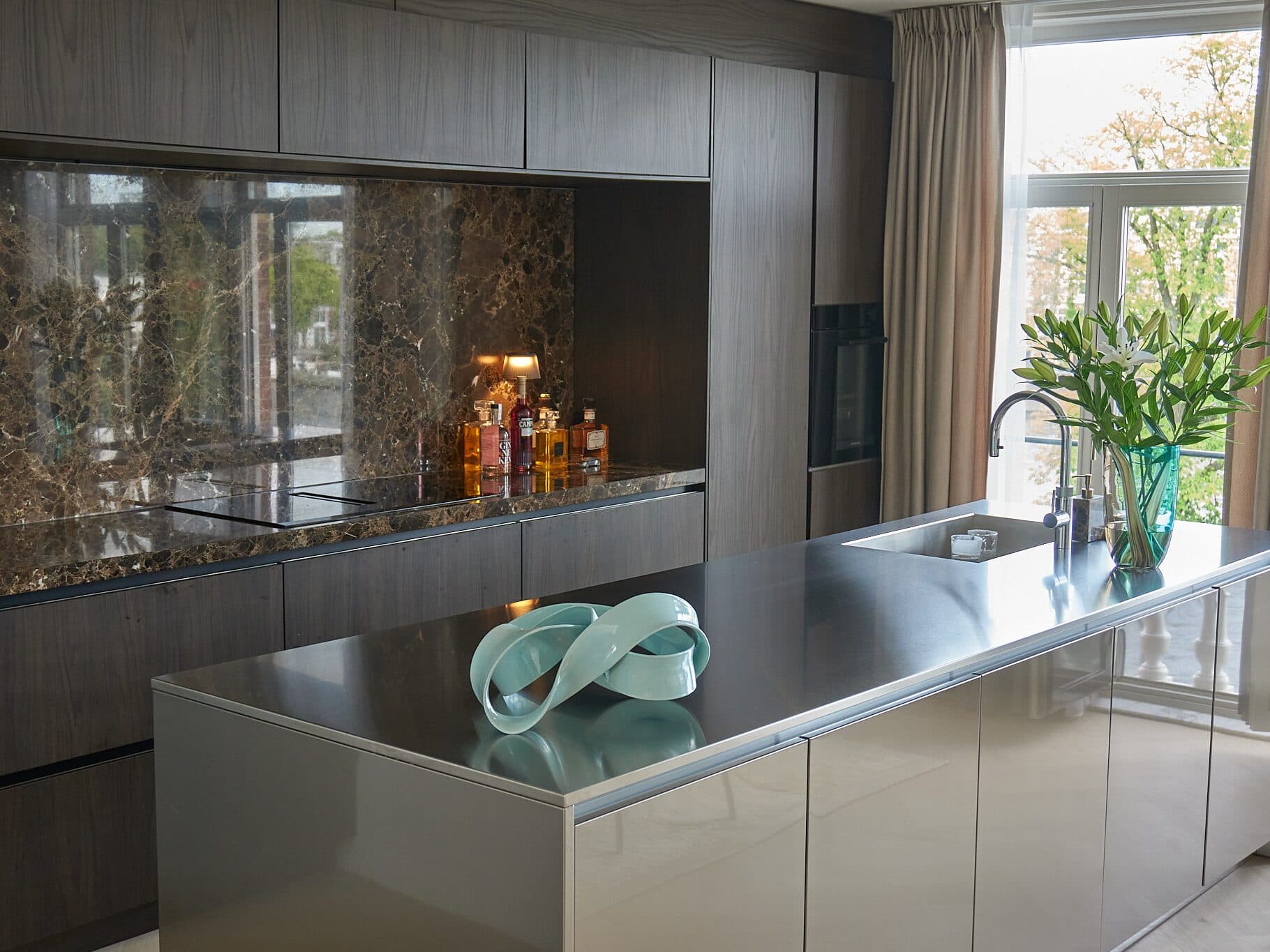 The same kitchen after L7M: dark oak, an Emperador marble splashback and a champagne metal island